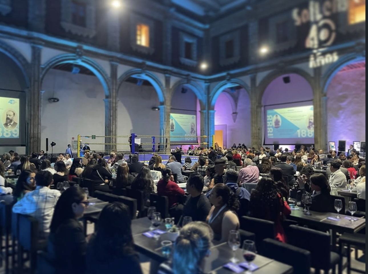 Salón histórico con mesas de invitados y un ring al fondo durante un evento corporativo