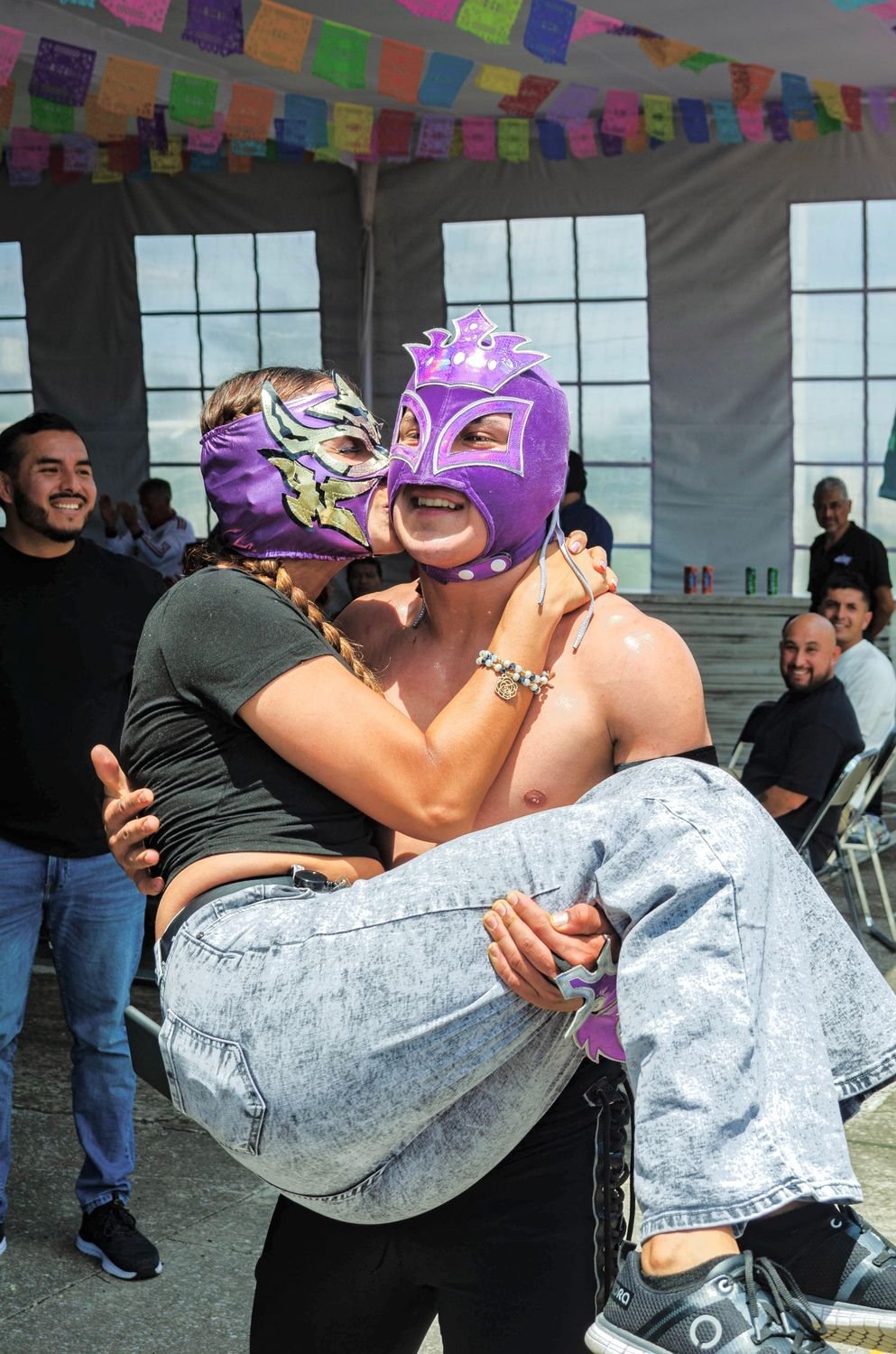 Luchador cargando a una asistente que lleva máscara de lucha libre