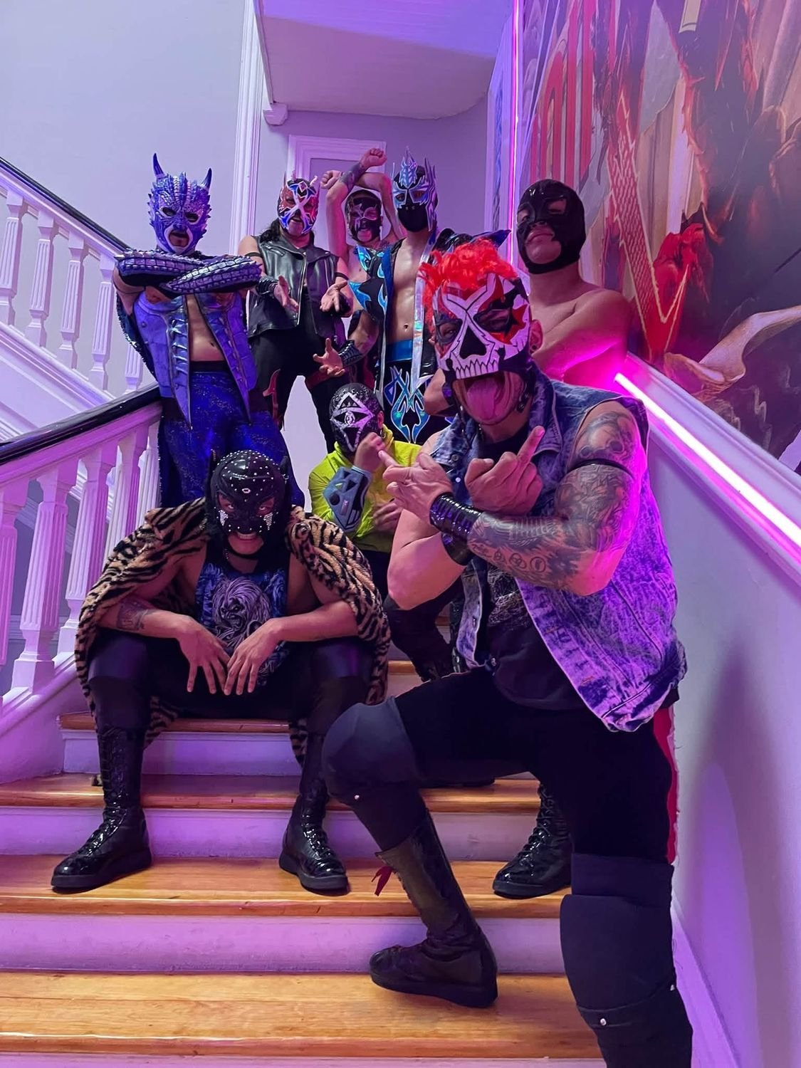 Grupo de luchadores enmascarados posando en una escalera con luces moradas
