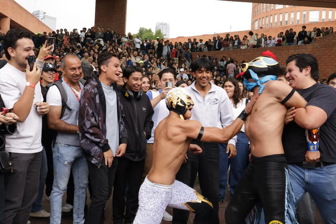 Luchadores entre el público en un evento al aire libre, con cientos de asistentes alrededor